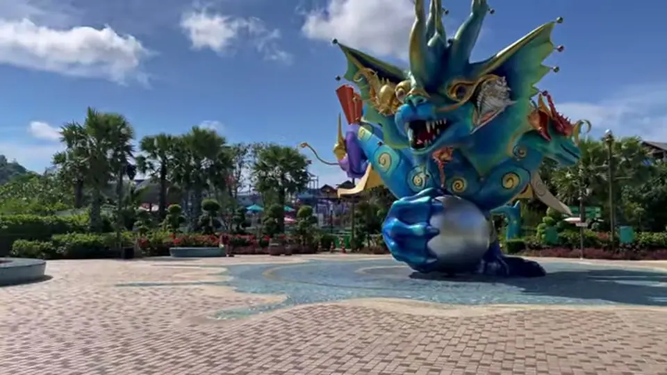 Giant blue dragon statue on a plaza among palms in daylight.