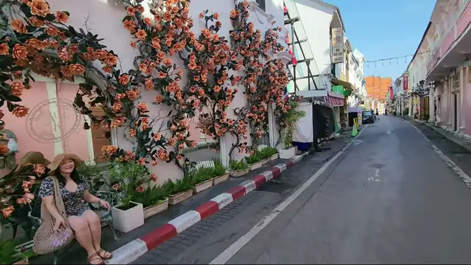 Woman in sunhat sits by a pink wall with orange flowers.