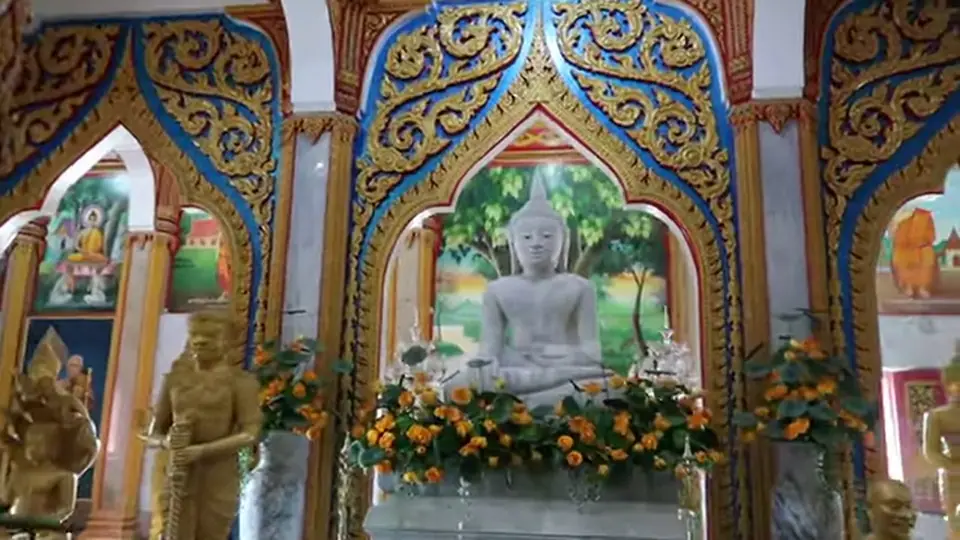 White Buddha statue on an altar within blue and gold arches.